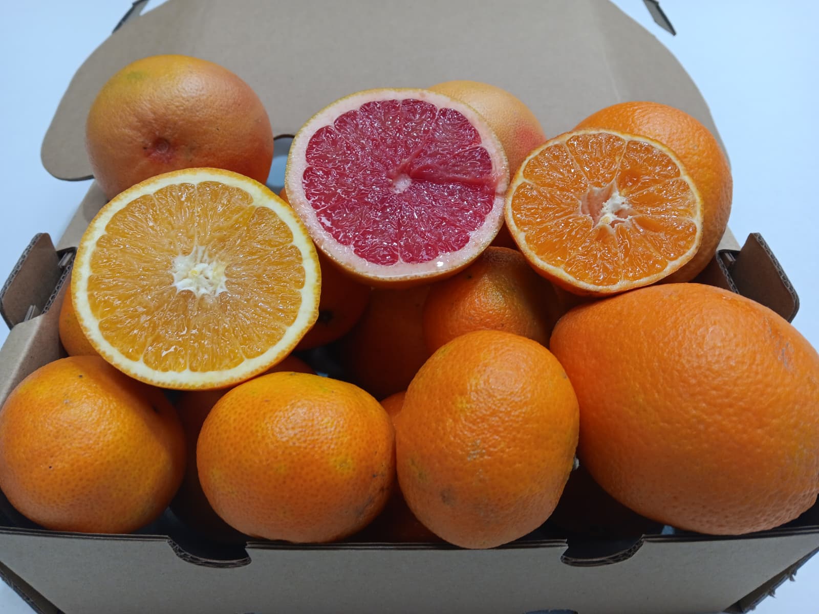 Caja de fruta ecológica con mandarinas, pomelos y naranjas recién recolectadas, con una naranja abierta mostrando su pulpa fresca.