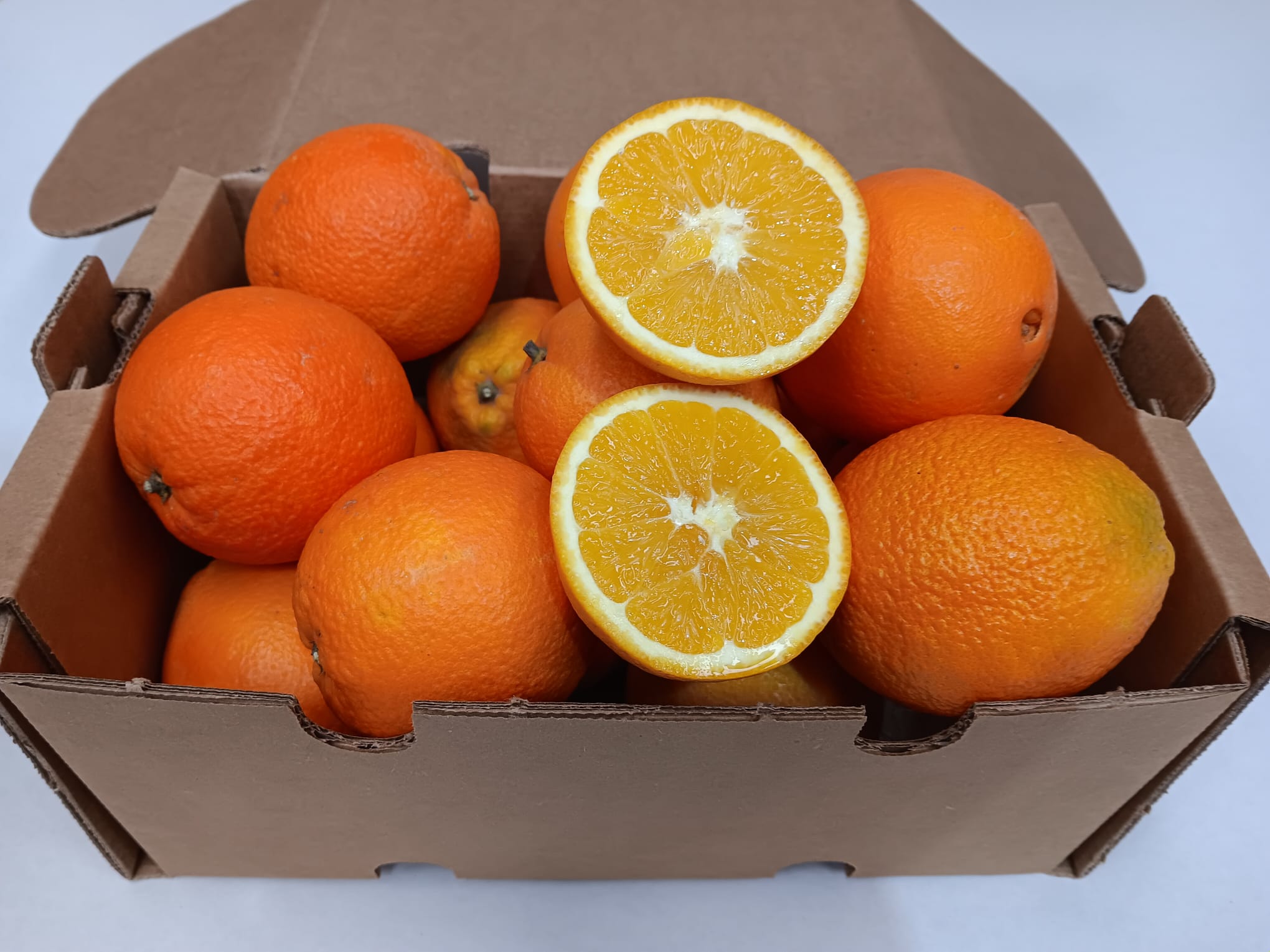 Caja de naranjas ecológicas recién recolectadas, con una naranja abierta mostrando su interior jugoso y natural.